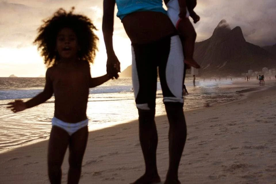 Criança e pessoa adulta de mãos dadas na areia da praia