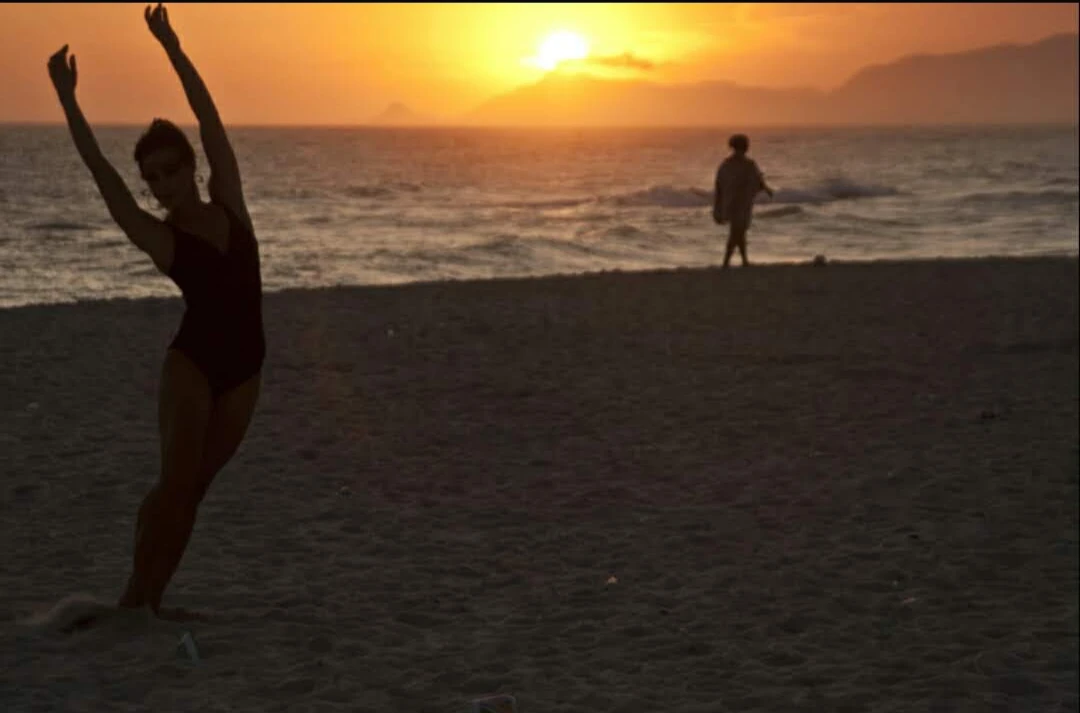 Silhuetas na areia e no mar diante do pôr do sol