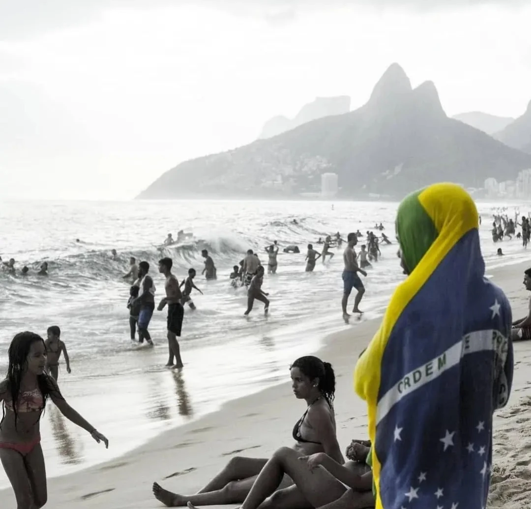 Pessoas na praia e tecido verde, amarelo e azul em primeiro plano